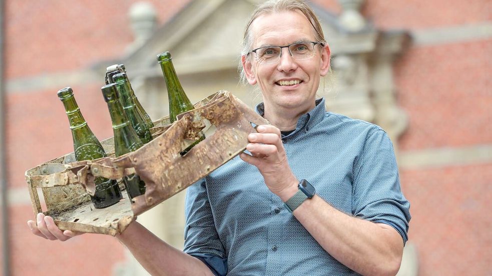 Der Blechbierkasten und die Flaschen, die Dr. Jan Kegler in die Kamera stemmt, sind Fundstücke aus der Ostfriesischen Actien-Brauerei Aurich. Foto: Ortgies