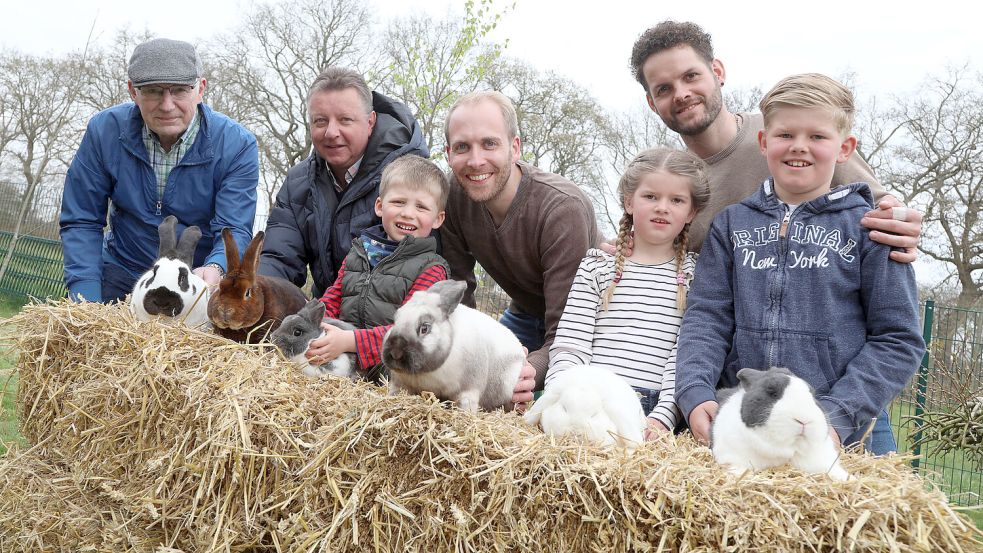 Herausputzen fürs Foto: Erster Vorsitzender Warner Behrends (von links), langjähriges Mitglied Georg Saathoff, zweiter Vorsitzender Ralf Adams und Jugendleiter Steffen Weber mit den Kindern Till, Efke und Meent. Zu sehen sind die Kaninchenrassen: Deutsche Riesenschecke schwarz-weiß (von links), Castor-Rexe, Farbenzwerg mantelgescheckt blau-weiß, Sallander, Zwergwidder weiß Blauauge und Holländer blau weiß. Foto: Romuald Banik