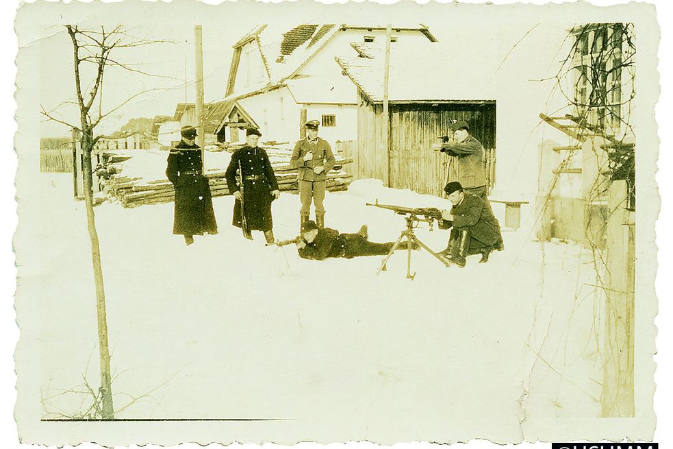 Trawniki bei demonstrativen Schießübungen im Hof der Kommandantur, angeleitet von Niemann (Mitte), Frühjahr 1942. Im Hintergrund ist ein weiteres Unterkunftsgebäude der Lagermannschaft sichtbar. In dem Holzschuppen zwischen Unterkunftsgebäude und Kommandantur wurde eine Zeit lang Brennholz aufbewahrt. Später wurde der Schuppen abgerissen.