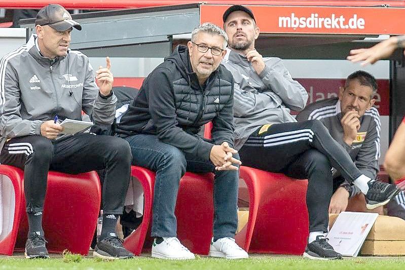 Unions Co-Trainer Markus Hoffmann, Trainer Urs Fischer und Co-Trainer Sebastian Bönig (l-r) sitzen auf Bank. Foto: Andreas Gora/dpa