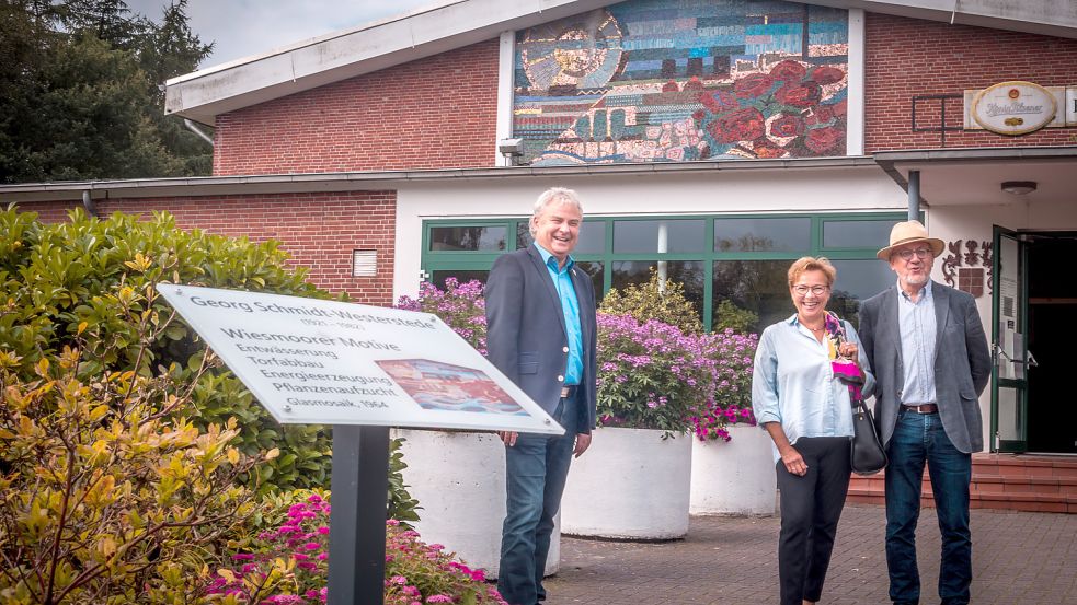 Der Wiesmoorer Bürgermeister Friedrich Völler (von links) freut sich gemeinsam mit den Künstler-Nachfahren Susann und Manfred Hylla über die Infotafel zum Glasmosaik an der Fassade des Hallenbades. Foto: Cordsen