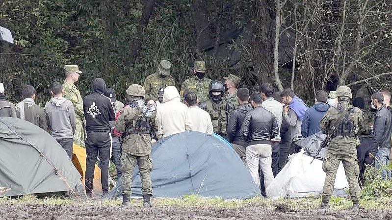 Migranten, die an der Grenze zu Belarus festsitzen, werden von polnischen Beamten umstellt. Foto: Czarek Sokolowski/AP/dpa