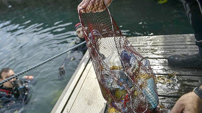 Ein Taucher hält ein Netz mit Abfällen, die er im baskischen Dorf Bermeo aus dem Meer entzogen hat. (Archivbild). Foto: Alvaro Barrientos/AP/dpa