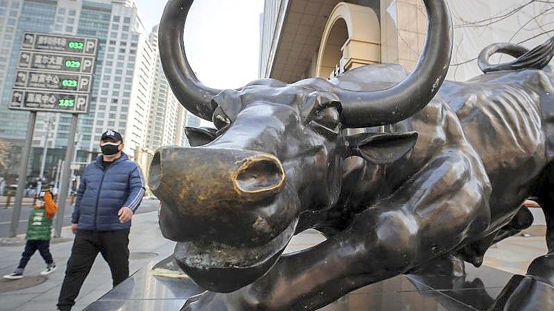 Menschen gehen an der Stier-Statue vor einem Bürogebäude in Peking vorbei. (Archivbild). Foto: Andy Wong/AP/dpa