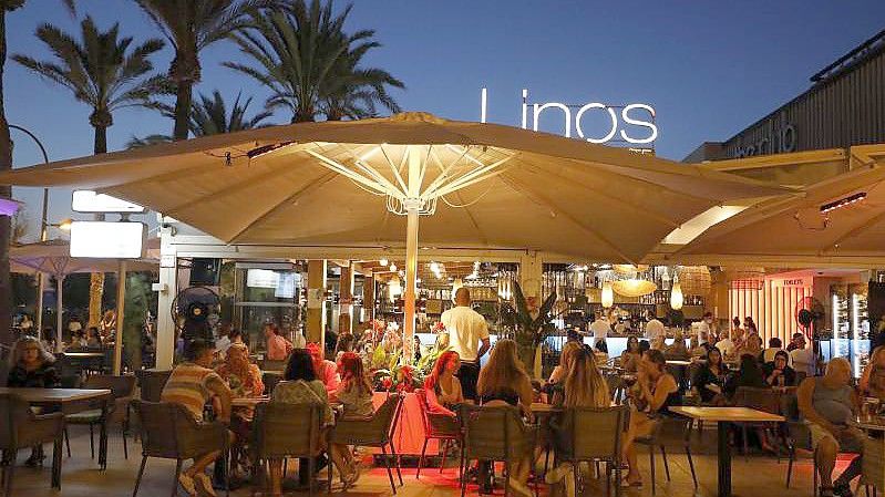 Menschen sitzen in einer Bar an der Strandpromenade von Palma. Foto: Clara Margais/dpa