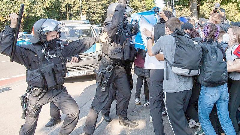 Ein Polizist hebt vor einer Gruppe von Demonstranten seinen Schlagstock. Foto: Peter Kneffel/dpa