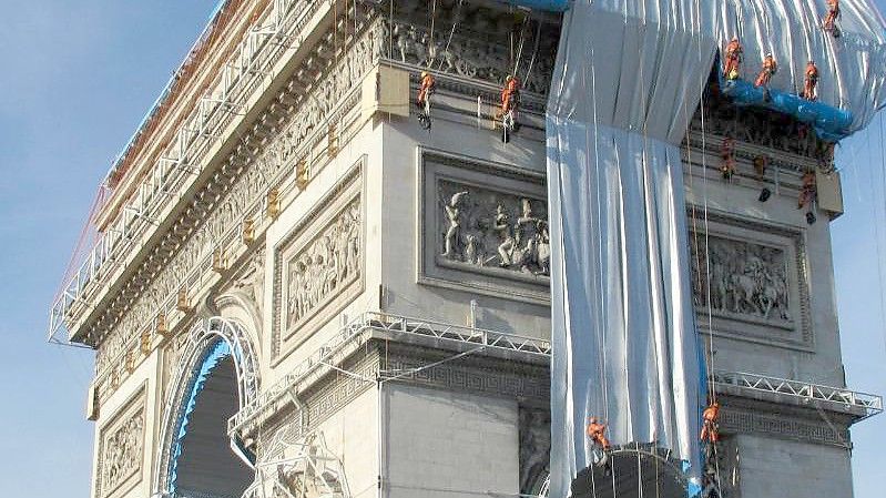 Gebäudekletterer haben mit der Verhüllung des Triumphbogens (Arc de Triomphe) begonnen. Foto: Sabine Glaubitz/dpa