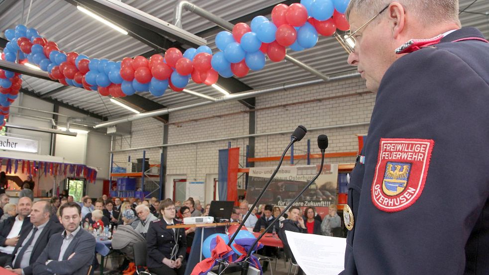 Karl-Heinz Berends spricht in der rot-blau dekorierten Fahrzeughalle zu den Mitgliedern der Feuerwehr Osterhusen und ihren Gästen. Foto: Päschel