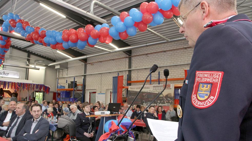 Karl-Heinz Berends spricht in der rot-blau dekorierten Fahrzeughalle zu den Mitgliedern der Feuerwehr Osterhusen und ihren Gästen. Foto: Päschel