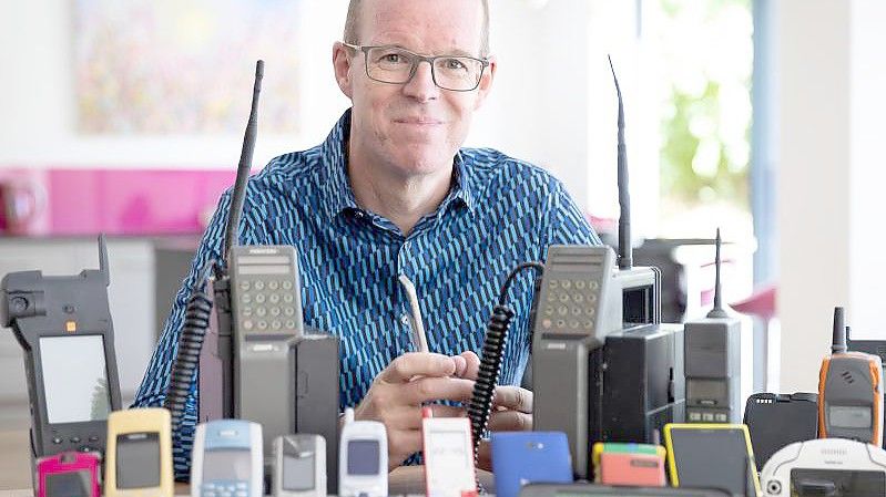 Auf dem vom Mobile Phone Museum herausgegebenen Foto sitzt Ben Wood, Gründer des Museums und Analyst des Unternehmens CCS Insight, hinter einigen der über 2.000 einzigartigen Mobiltelefone, die Teil des Online-Museums sein werden. Foto: Mobile Phone Museum/Vodafone/PA Media/dpa