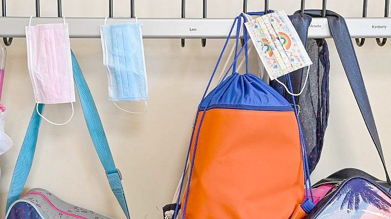 Masken hängen zusammen mit Taschen und Rucksäcken an Kleiderhaken in einem Klassenraum einer Grundschule. (Archivbild). Foto: Patrick Pleul/dpa-Zentralbild/dpa