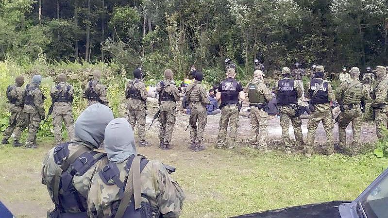 Migranten sitzen nach dem Grenzübertritt von Belarus nach Polen hinter Sicherheitskräften. Foto: Mateusz Wodziński/AP/dpa