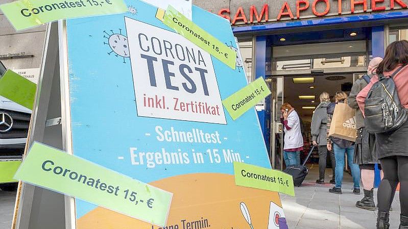 Passanten stehen in der Münchner Innenstadt vor einer Apotheke, die Coronatest für 15 Euro anbietet. Foto: Peter Kneffel/dpa