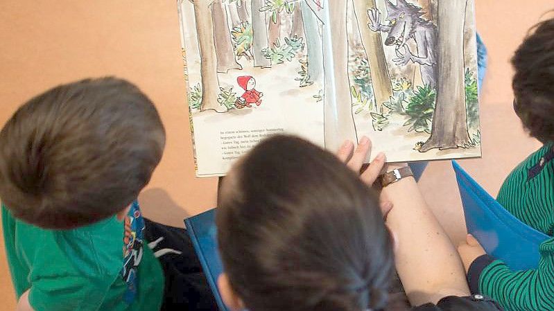 Eine Frau liest Kindern aus einem Buch vor. Foto: Arno Burgi/dpa-Zentralbild/dpa