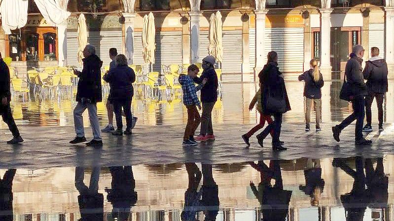 Menschen gehen über den überfluteten Markusplatz. Foto: Matteo Tagliapietra/LaPresse/AP/dpa