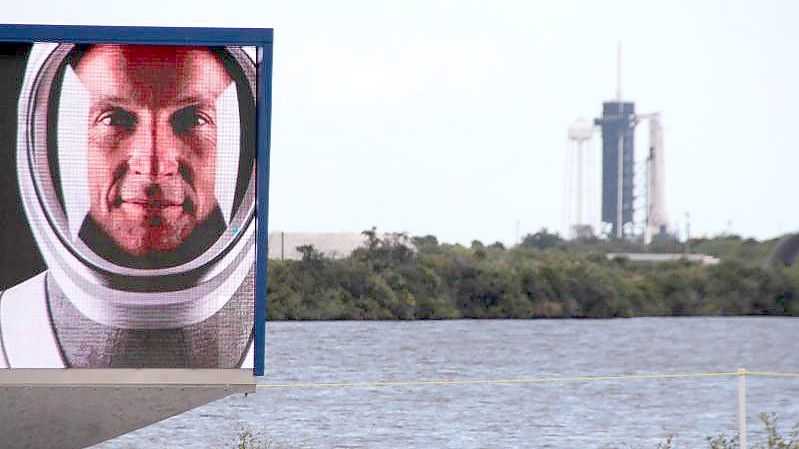 Matthias Maurer auf einem Video-Bildschirm vor dem Launchpad 39A in Cape Canaveral, an dem schon die Falcon-9-Rakete mit Crew Dragon-Kapsel aufgestellt ist. Foto: Christina Horsten/dpa