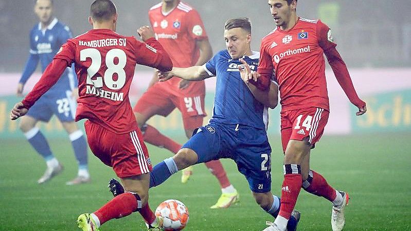 Der Karlsruher Marco Thiede (M) kämpft mit den Hamburgern Miro Muheim (l) und Ludovit Reis um den Ball. Foto: Uli Deck/dpa