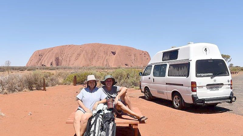 Menekse (l) und James Humphrey neben ihrem Van und vor dem Uluru (Ayers Rock) im Outback Australiens. Foto: Menekse Humphrey/@putteringaroundtheworld/dpa