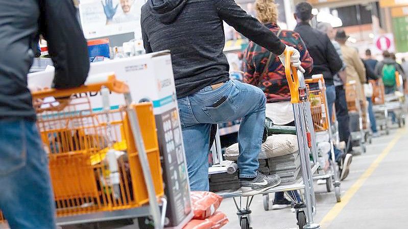 Kunden stehen mit Einkaufswagen in einem Baumarkt in einer Schlange vor den Kassen an. Die globalen Verwerfungen in den Lieferketten setzen Deutschlands Bau- und Gartenmärkte unter Druck. Foto: Sven Hoppe/dpa