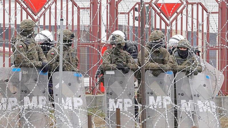 Polnische Sicherheitskräfte stehen hinter dem Grenzzaun am Grenzübergang Brusgi (Belarus) und Kuznica (Polen). Foto: Ulf Mauder/dpa