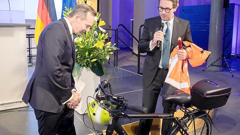 Volker Wissing (FDP, l), Bundesminister für Verkehr und Digitales, nimmt von Andreas Scheuer (CSU), scheidender Bundesminister für Verkehr und digitale Infrastruktur, bei der Amtsübergabe im Bundesministerium für Verkehr und Digitales einen Fahrradhelm und weitere Ausrüstung entgegen. Foto: Christoph Soeder/dpa