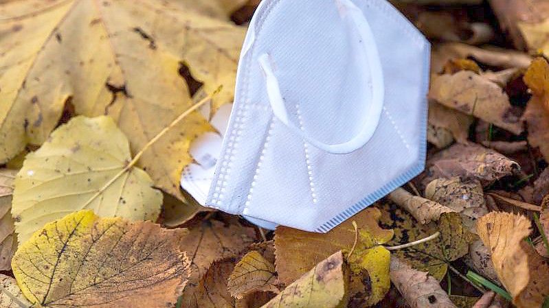 Eine Mund-Nasen-Bedeckung liegt im herbstlichen Laub im Englischen Garten in München. Foto: Peter Kneffel/dpa
