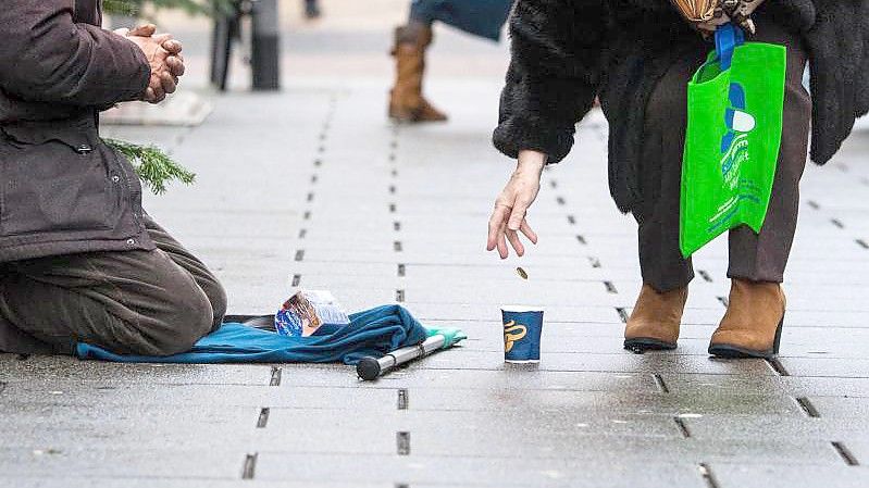 Eine Frau wirft einem Bettler in einer Einkaufsstraße ein Geldstück in einen Becher. Foto: Andreas Arnold/dpa