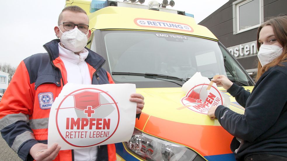Tobias Johannes, Notfallsanitäter beim RKSH, und Jasmin Baar von der Emder Werbeagentur Noosten, bekleben einen Rettungswagen mit der Botschaft: „Impfen rettet Leben!“. Foto: Päschel