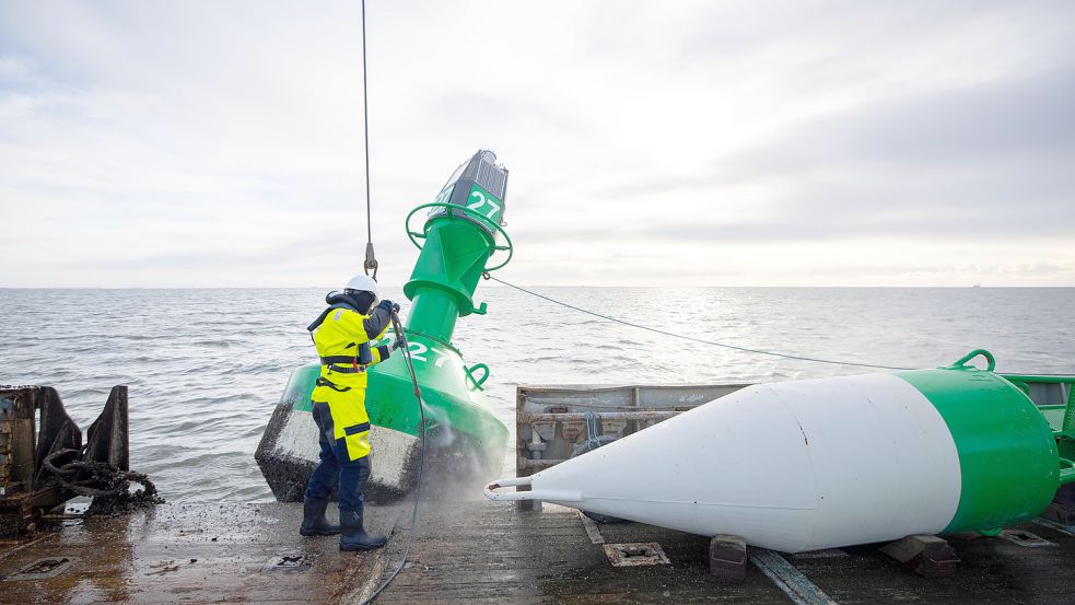 Ein Mitarbeiter auf dem Tonnenleger „Triton“ reinigt die Fahrwassertonne 27, bevor die schlankere Wintertonne (rechts) im Fahrwasser Süderpiep vor Büsum in die Nordsee gelassen wird. Foto: Charisius, dpa