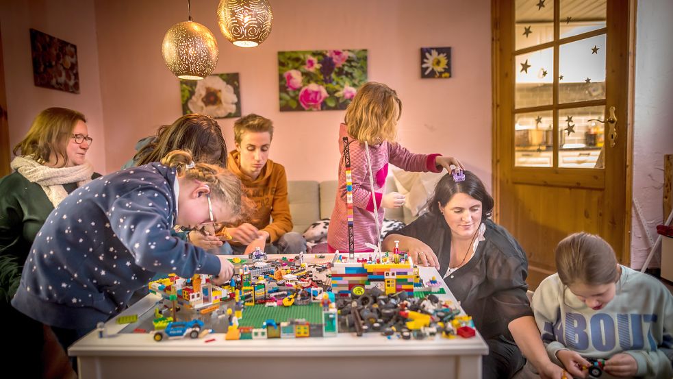 Die Vollmers – Angelika (von links), Finja, Aylin (verdeckt), Philipp, Molly, Yasmin und Lini – spielen am mit Lego überhäuften Wohnzimmertisch. Foto: Cordsen