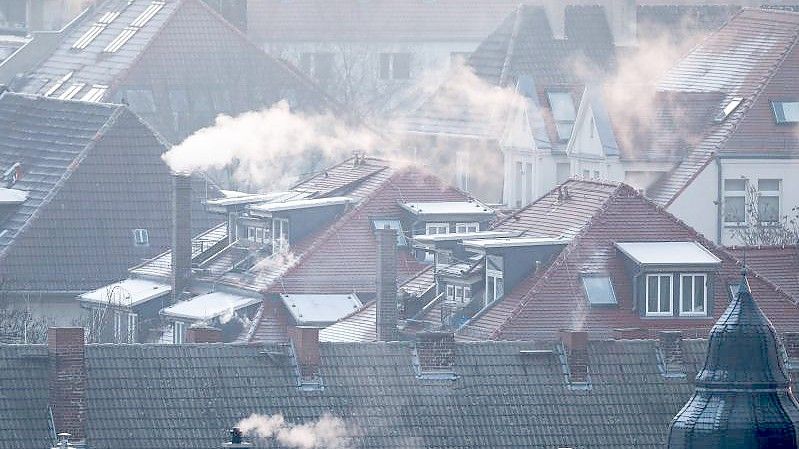 Rauch steigt aus den Kaminen auf den Dächern von Mehrfamilienhäusern an einem kalten Wintermorgen. Foto: Jan Woitas/dpa