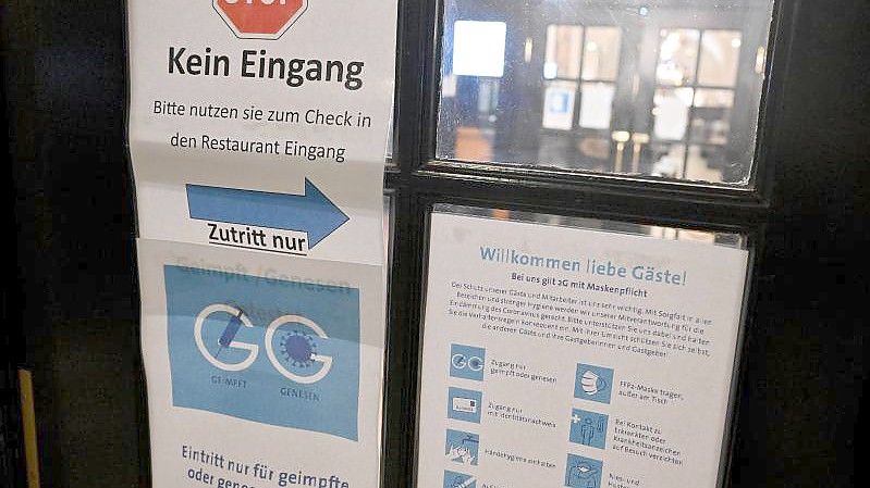Diverse Schilder zum Einhalten der Corona-Schutzmaßnahmen hängen am Eingang zu einer Gaststätte. Foto: Peter Kneffel/dpa