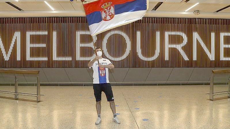 Ein Fan des serbischen Tennisspielers Novak Djokovic schwenkt in der Ankunftshalle des Flughafens Melbourne eine serbische Fahne. Foto: Hamish Blair/AP/dpa
