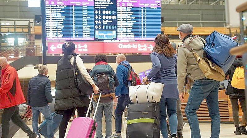 Reisende stehen am Flughafen BER vor einer Info-Tafel. Foto: Joerg Carstensen/dpa