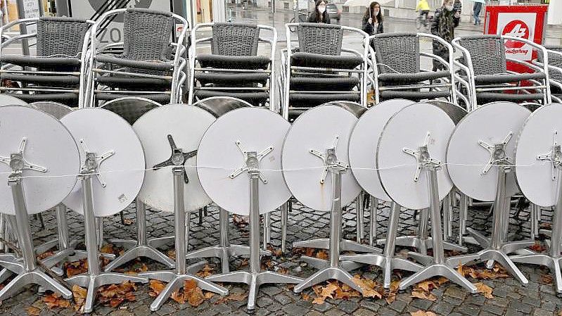 Zusammengestellte Stühle und Tische stehen vor einem Café in München. Foto: Peter Kneffel/dpa