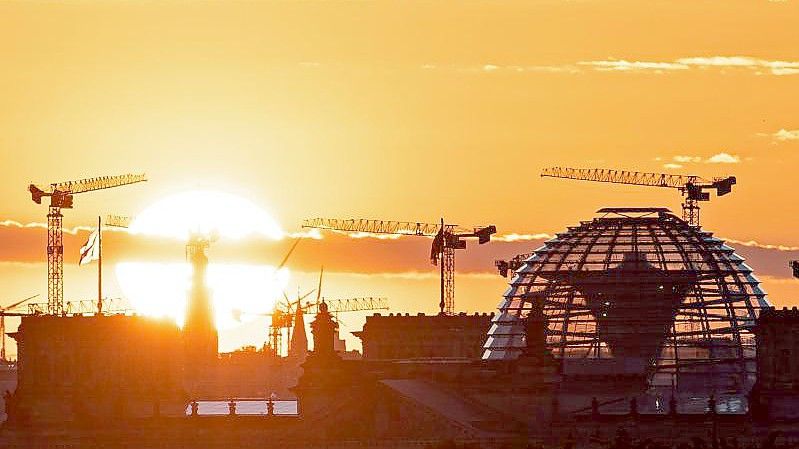 Baukräne und die Kuppel des Reichstagsgebäudes in Berlin. Die deutsche Wirtschaft kommt wieder in Schwung. Foto: Fabian Sommer/dpa