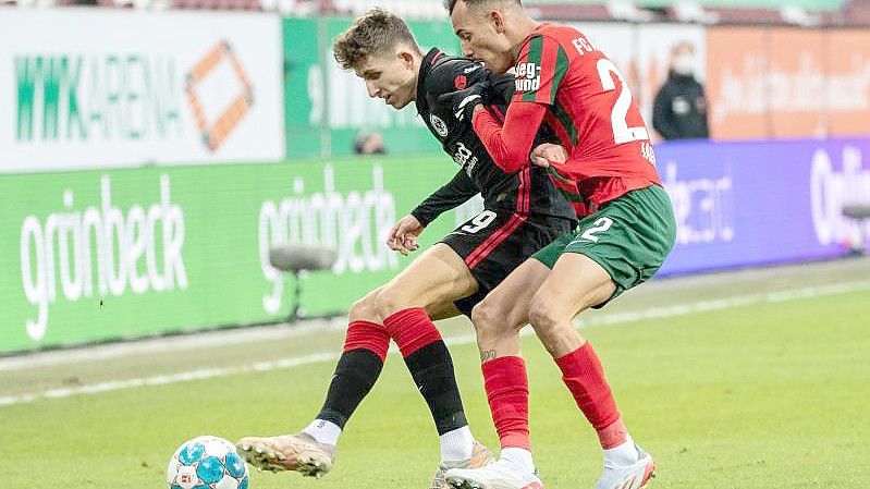 Jesper Lindström von Eintracht Frankfurt (l) und Iago von Augsburg kämpfen um den Ball. Foto: Matthias Balk/dpa
