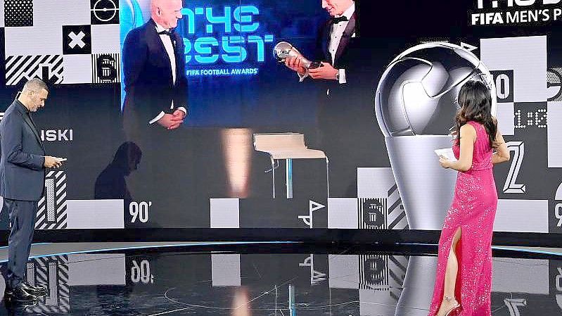 Dem FCB-Stürmer Robert Lewandowski (r. auf Bildschirm) wird 2020 die Weltfußballer-Trophäe überreicht. Foto: Valeriano Di Domenico/POOL FIFA/Getty/dpa