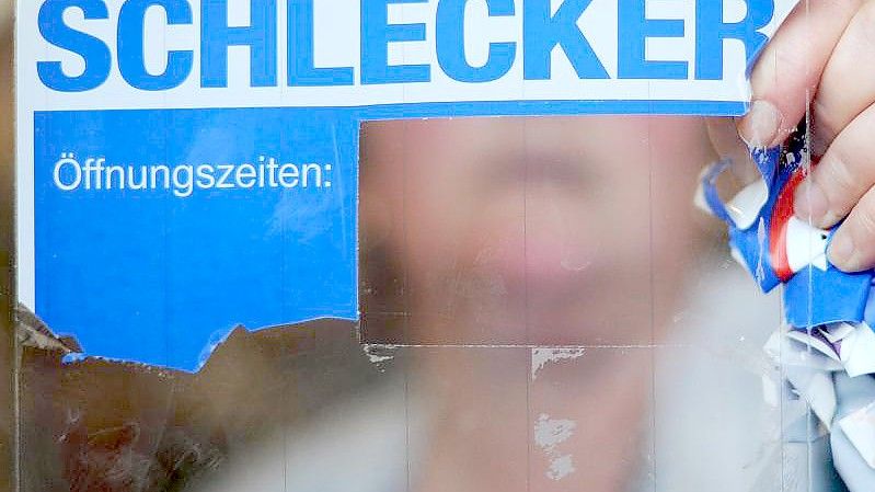 Eine Schlecker-Mitarbeiterin reißt das Firmenlogo von der Eingangstür einer Filiale. Foto: picture alliance / Julian Stratenschulte/dpa