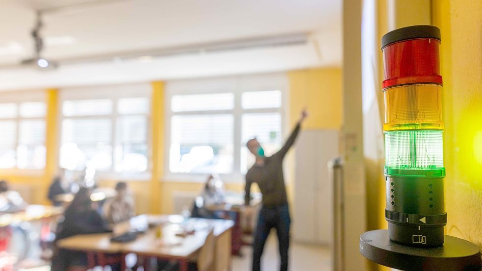 Eine Luftqualitätsampel in einem Klassenzimmer leuchtet grün während im Hintergrund ein Lehrer unterrichtet. Mit solchen Warnsystemen und Luftentkeimern kann der Infektionsschutz an Schulen verbessert werden. Foto: Philipp von Ditfurth/DPA