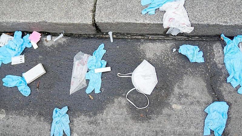 Einmalhandschuhe, FFP2-Maske und benutzte Corona-Antigen-Testkits liegen auf der Straße vor einem Corona-Testzentrum. Foto: Kay Nietfeld/dpa