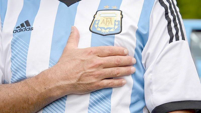 Ein Mann, der ein Trikot der argentinischen Nationalmannschaft trägt, legt sein Hand aufs Herz. (Archivbild). Foto: Julieta Ferrario/dpa