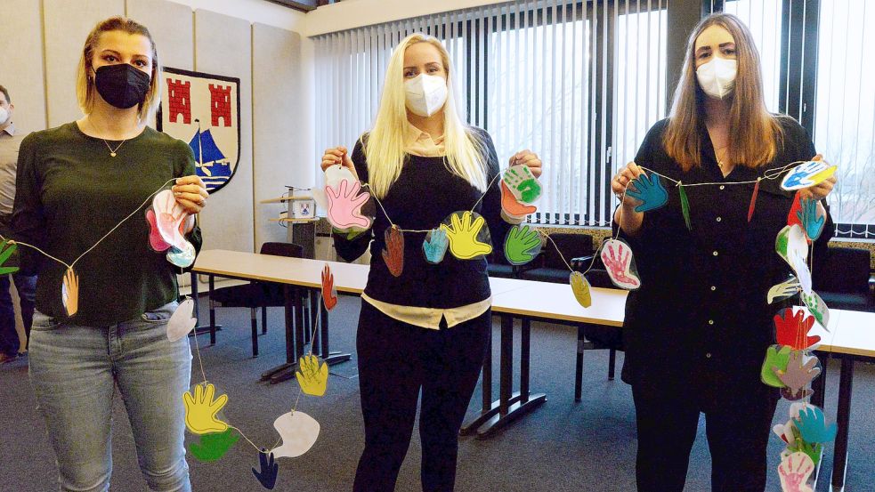 Um zu zeigen, wie viele Kinder auf den neuen Kindergarten in Warsingsfehn warten, haben (von links) Denise von Rahden, Dana Göbel und Anneke Schüür eine Kette aus Handabdrücken der Krippenkinder mit ins Rathaus gebracht. Foto: Lüppen