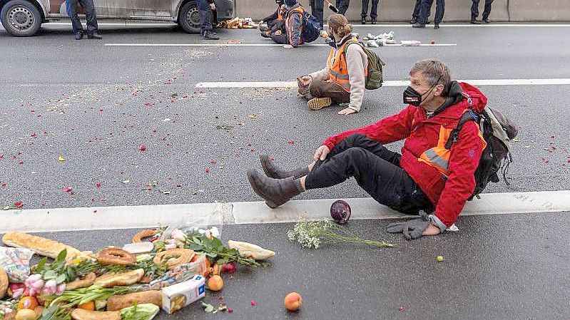 Klimaaktivisten der Gruppe „Aufstand der letzten Generation“ sitzen auf der Fahrbahn und blockieren den Verkehr. Foto: Carsten Koall/dpa