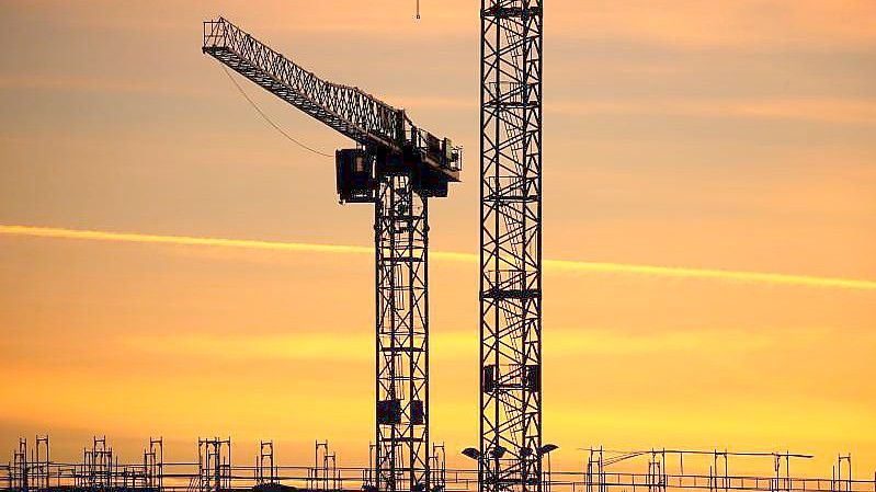 Baukräne einer Großbaustelle stehen im Sonnenaufgang. Der Deutsche Industrie- und Handelskammertag hat seine Wachstumsprognose für 2022 gesenkt. Foto: Karl-Josef Hildenbrand/dpa