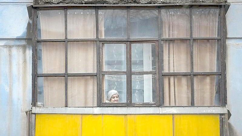 Eine Frau blickt aus dem Fenster eines Hauses in Sjewjerodonezk im Osten der Ukraine. Foto: Vadim Ghirda/AP/dpa