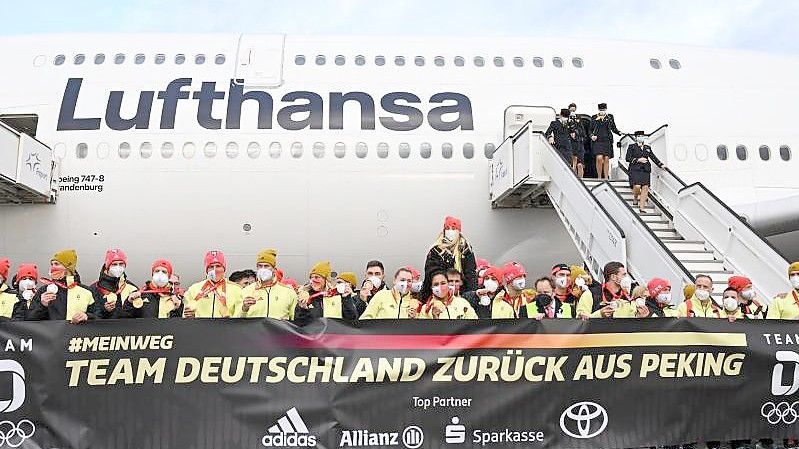 Das deutsche Olympia-Team steht bei der Rückkehr von den Winterspielen auf dem Frankfurter Flughafen hinter einem Plakat: „Team Deutschland zurück aus Peking“. Foto: Arne Dedert/dpa