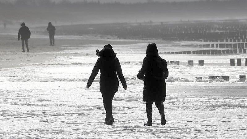 Spaziergänger laufen am Ostseestrand in Wustrow entlang - dort sorgte Sturmtief "Antonia" für dunklen Himmel und aufgeschäumtes Wasser. Foto: Bernd Wüstneck/dpa-Zentralbild/dpa