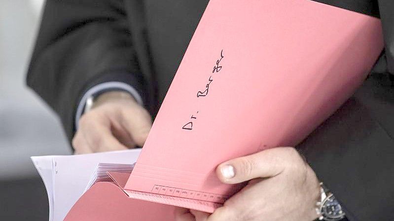 Ein Rechtsanwalt des Hauptbeschuldigten Hanno Berger hält vor dem Prozessauftakt um „Cum-Ex“-Aktiendeals im Gerichtssaal eine Akte mit der Aufschrift „Dr. Berger“ in der Hand. Foto: Boris Roessler/dpa