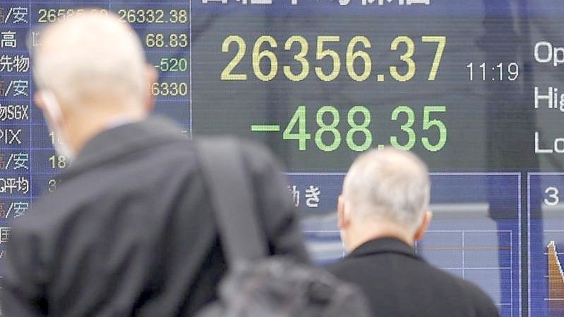 Menschen mit Mund-Nasen-Schutz gehen an einer elektronischen Börsentafel vorbei, die den japanischen Nikkei-Aktienindex anzeigt. Foto: Rodrigo Reyes Marin/ZUMA Press Wire/dpa